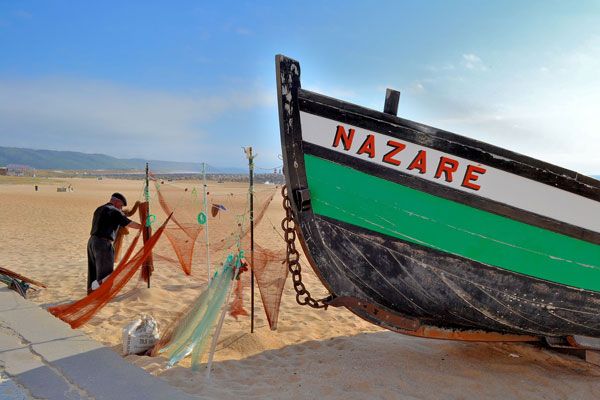 Fisherman fixing fishing nets next to traditional fishing boat in Nazare Portugal